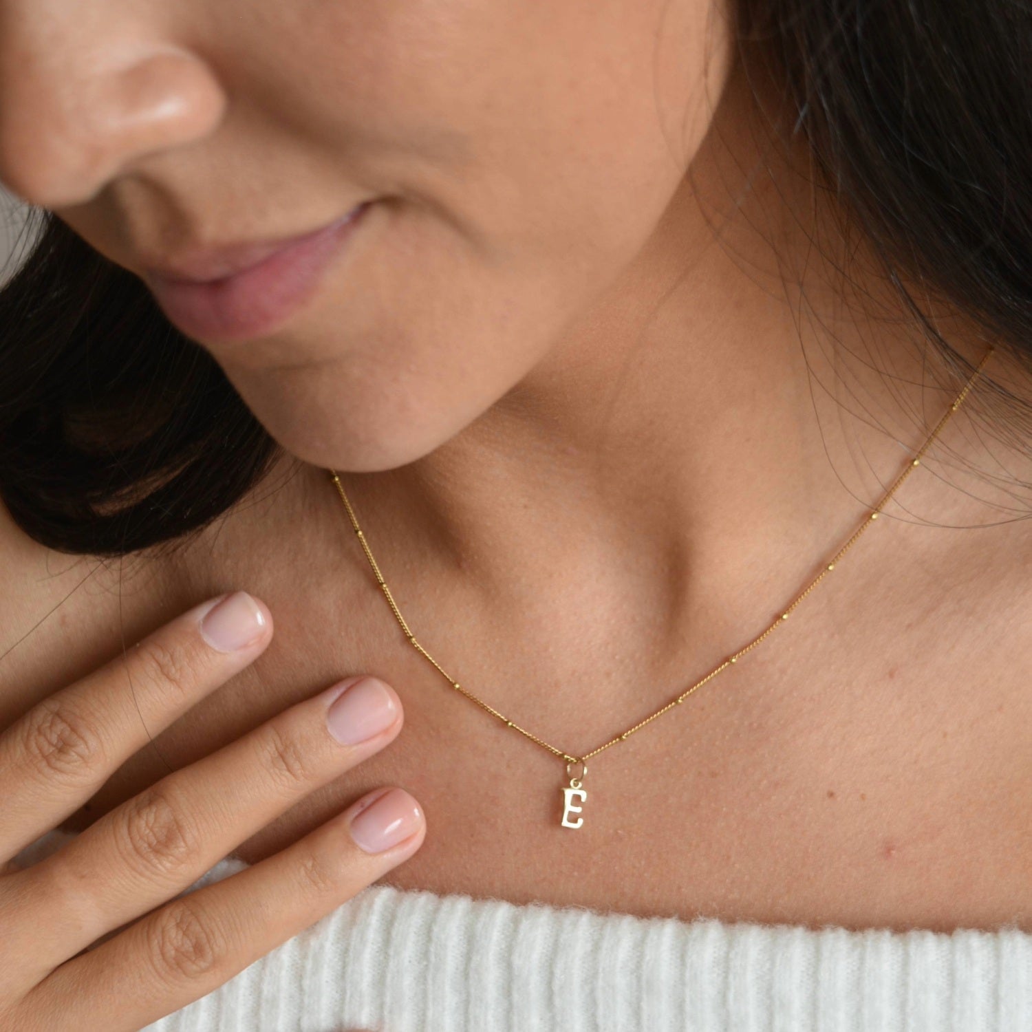 9ct solid gold initial pendant on a fine chain, worn at the neckline with a hand resting beside the necklace.