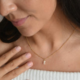9ct solid gold initial pendant on a fine chain, worn at the neckline with a hand resting beside the necklace.
