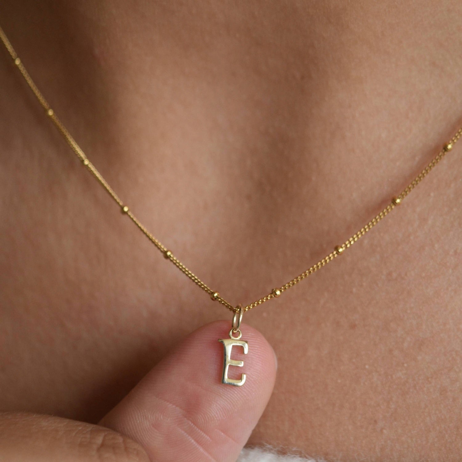 9ct solid gold initial pendant held between fingertips while worn, showing the letter charm’s size and detail.