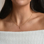 9ct solid gold initial necklace worn above a pale ribbed top, showing where the pendant sits below the collarbone.
