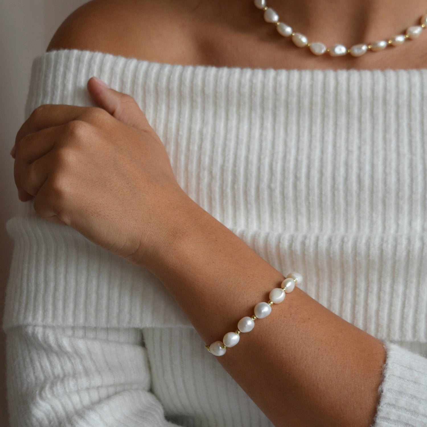Aliya gold and ivory baroque pearl bracelet worn on the wrist, with the arm resting across a pale ribbed top.
