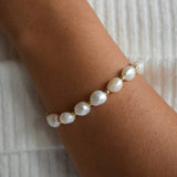 Close-up of the Aliya bracelet on the wrist, showing irregular ivory baroque pearls alternating with small gold details.