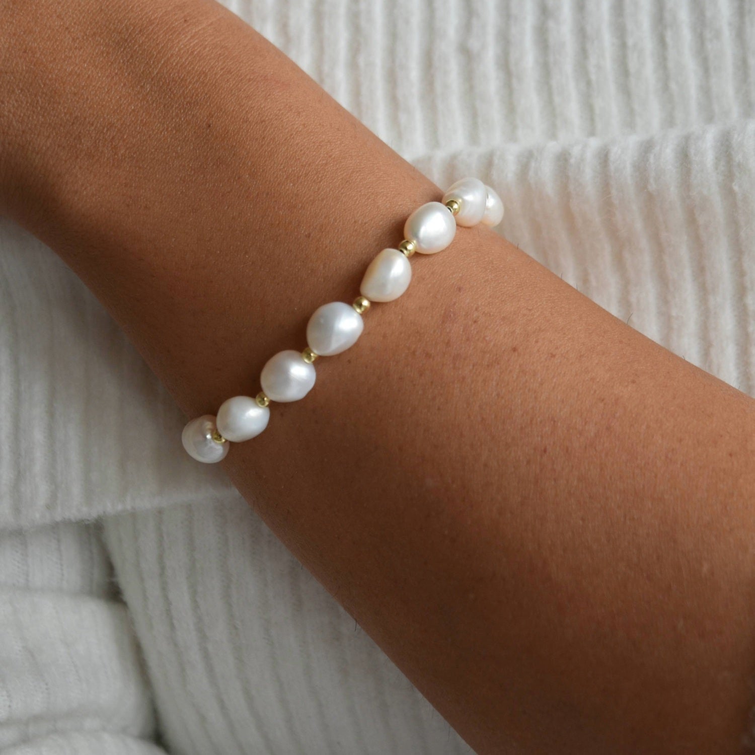 Angled view of the Aliya gold and ivory baroque pearl bracelet, showing how the pearls sit around the wrist.