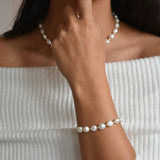 Aliya ivory baroque pearl bracelet with gold details, worn on a raised wrist with the hand resting near the neckline.