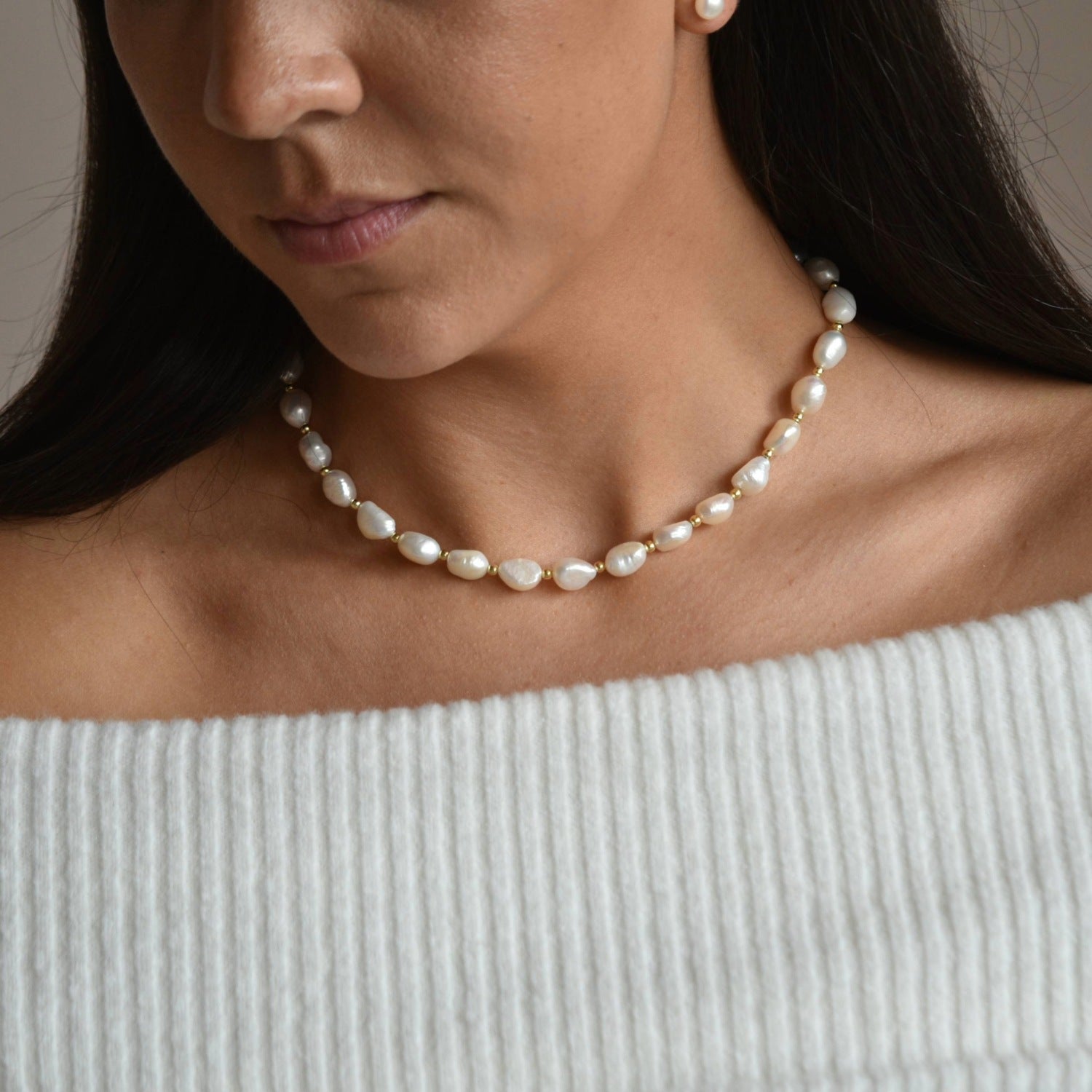 Aliya ivory baroque pearl necklace with gold vermeil details, shown on a model looking down towards the necklace.