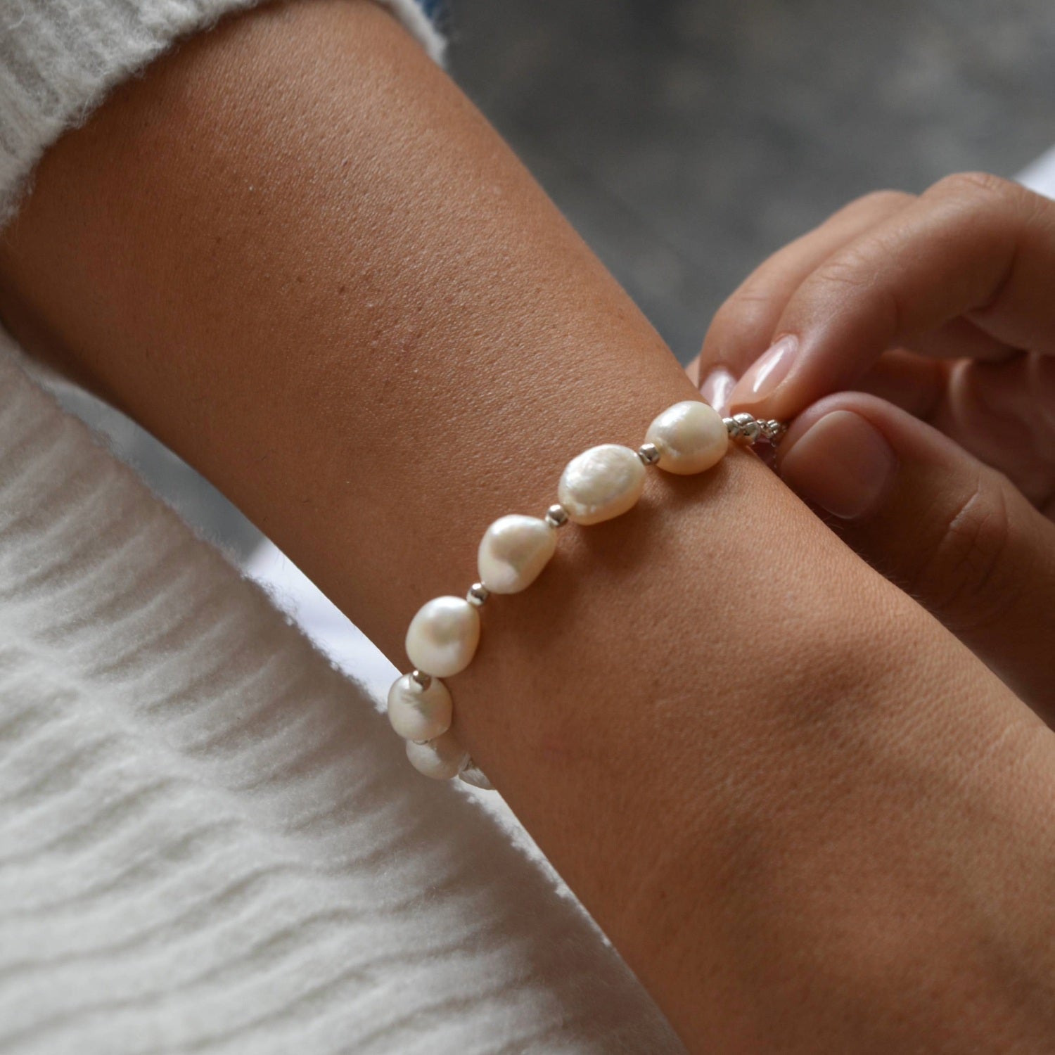 Close-up of the Aliya sterling silver bracelet, with fingertips beside the irregular ivory baroque pearls.