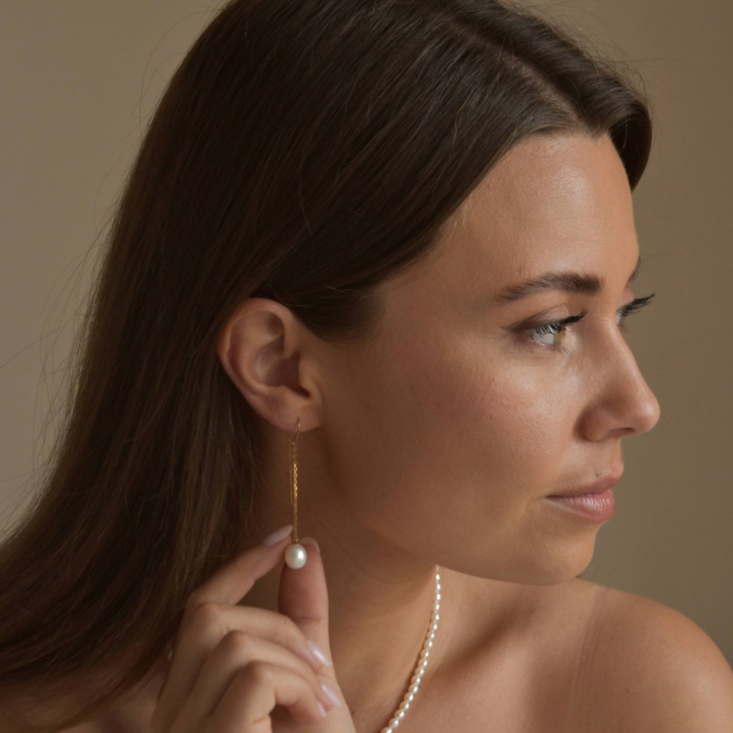 Gold vermeil ivory pearl threader earrings shown on a model in profile, with her hand resting near her neck.