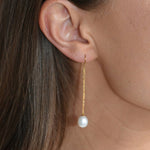 Close-up of a gold vermeil threader earring, showing its fine chain and ivory pearl drop against the skin.