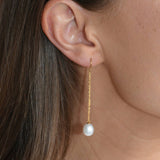 Close-up of a gold vermeil threader earring, showing its fine chain and ivory pearl drop against the skin.