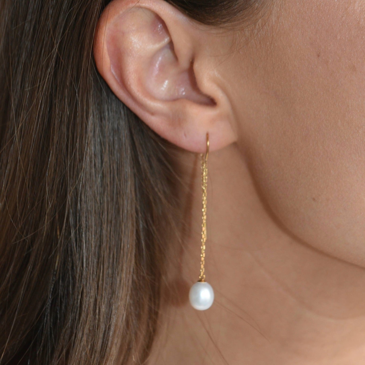 Close-up of a gold vermeil threader earring, showing its fine chain and ivory pearl drop against the skin.