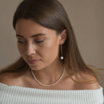 Gold vermeil ivory pearl threader earrings worn by a model looking down, showing their length beside the face.