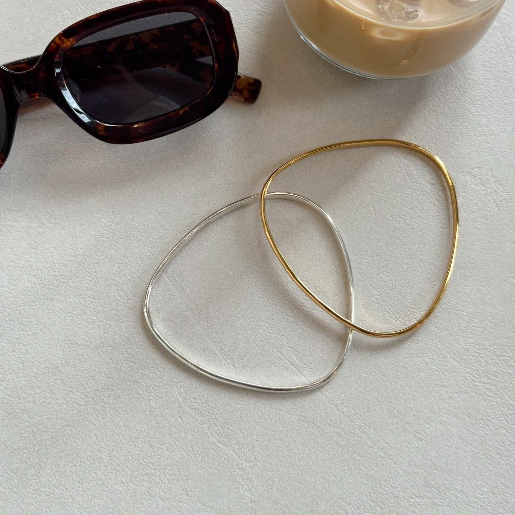 Gold vermeil and sterling silver Signature Bangles beside sunglasses and a coffee