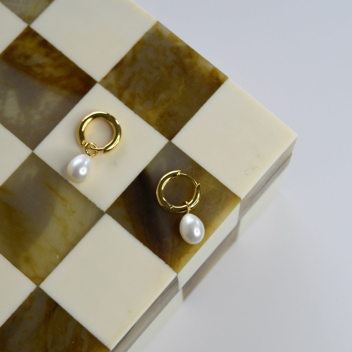 Gold vermeil huggie earrings with freshwater pearl drops on a chequered tray