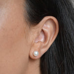 Close-up of a large ivory pearl button stud earring worn on the ear, showing its rounded shape and lustre.