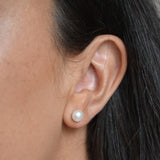 Close-up of a large ivory pearl button stud earring worn on the ear, showing its rounded shape and lustre.