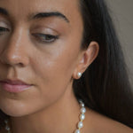 Large ivory pearl button stud earrings worn by a model, showing their size and appearance alongside the face.
