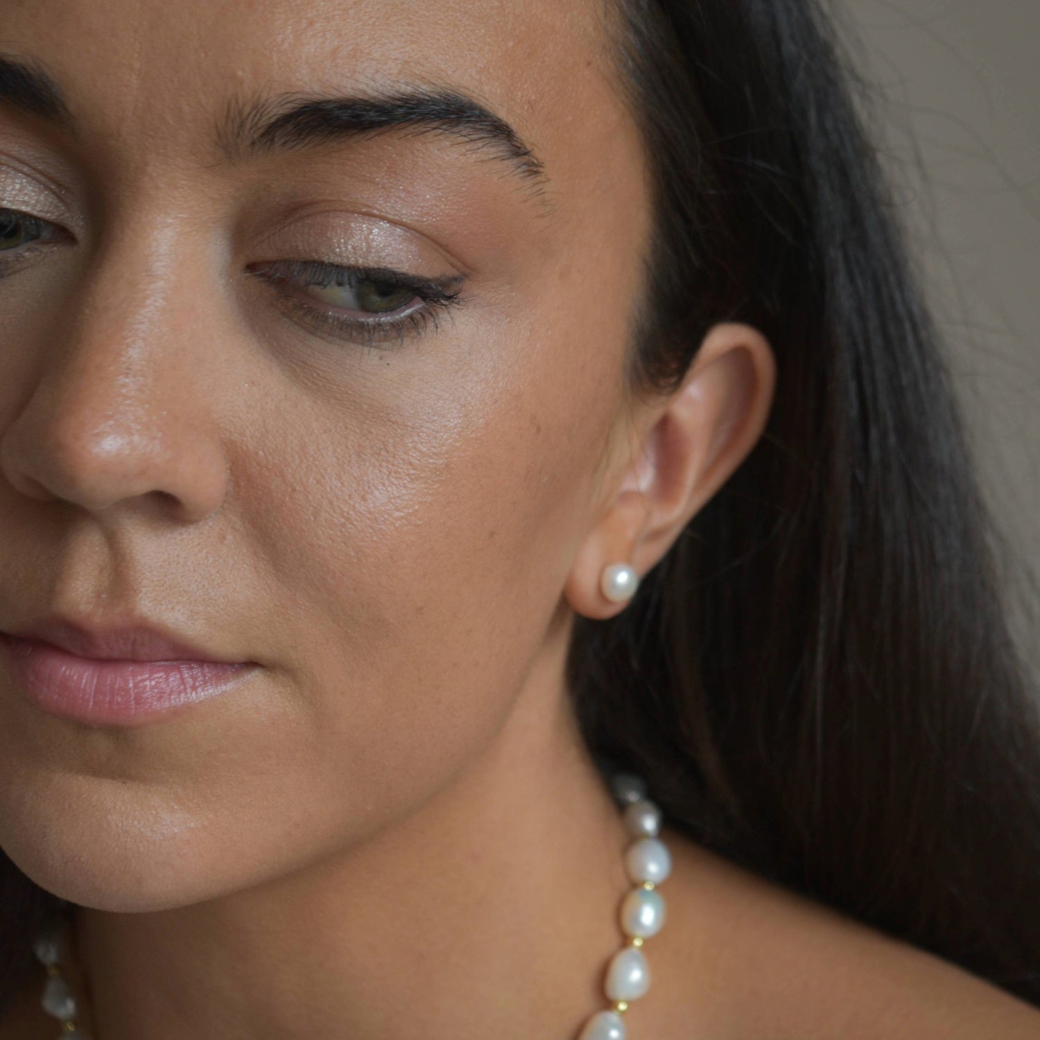 Large ivory pearl button stud earrings worn by a model, showing their size and appearance alongside the face.