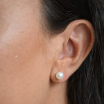 Angled close-up of an ivory pearl button stud earring, showing how the pearl sits against the earlobe.