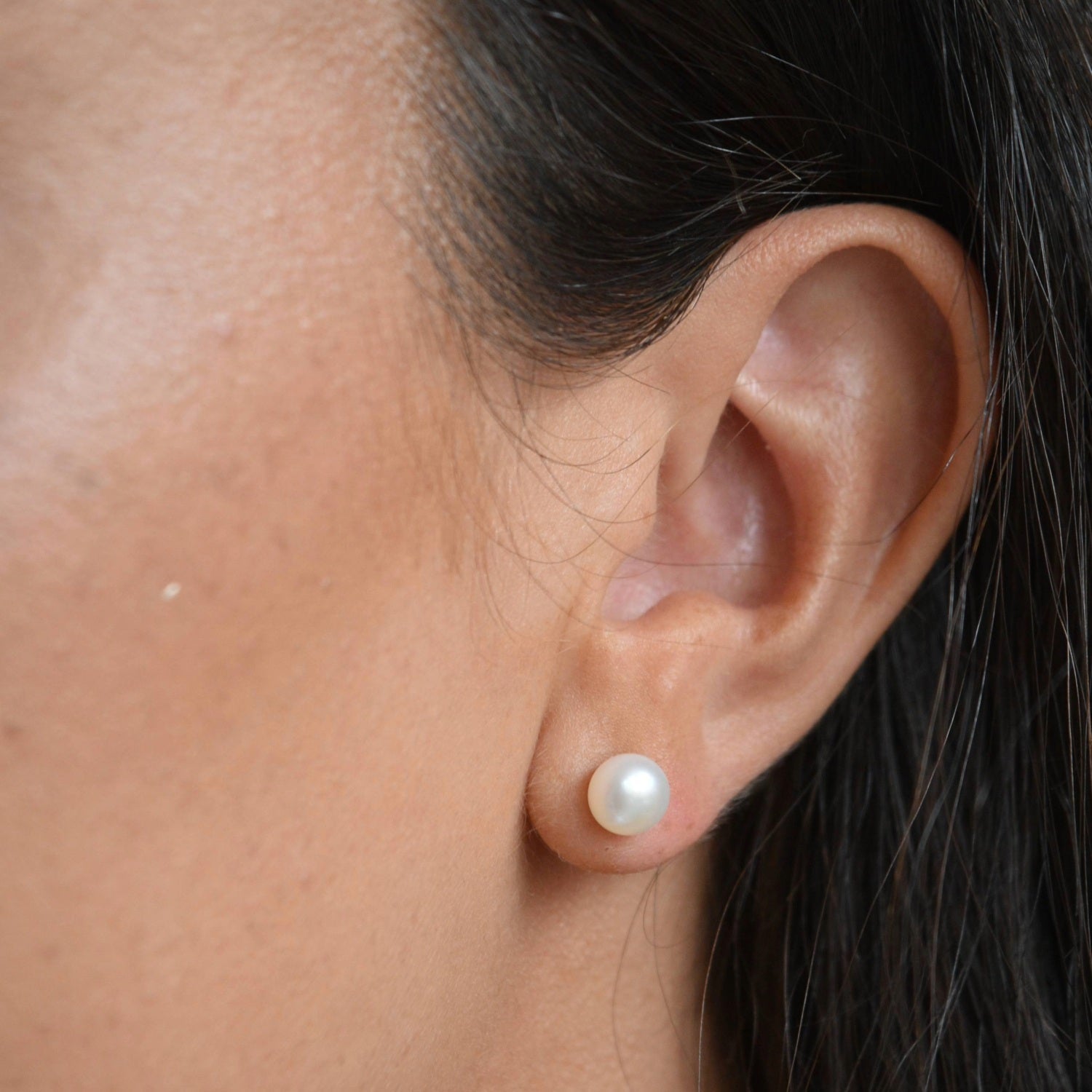 Angled close-up of an ivory pearl button stud earring, showing how the pearl sits against the earlobe.