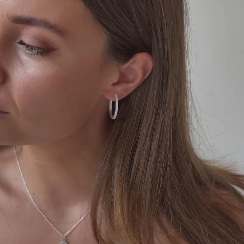 a model wearing a pair of sterling silver medium sized cz hoop earrings 