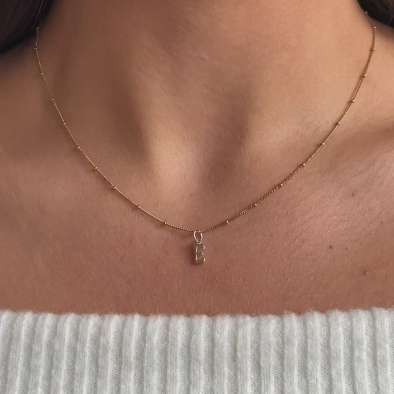 a model wearing a solid gold initial letter charm necklace on a satellite chain necklace 