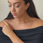 a model wearing a set of gold vermeil jewellery. A delicate gold paperclip chain link necklace, a delicate gold st Christopher pendant necklace and a gold paperclip link bracelet 