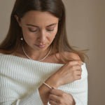 Riya sterling silver ivory seed pearl bracelet shown on a model looking down, with her other hand supporting her wrist.