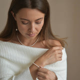 Riya sterling silver ivory seed pearl bracelet shown on a model looking down, with her other hand supporting her wrist.