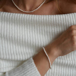 Riya sterling silver ivory seed pearl choker necklace worn close to the neck above an off-the-shoulder top.