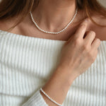 Riya ivory seed pearl choker with sterling silver details, worn with a matching bracelet and a hand near the shoulder.