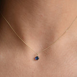 Solid 9ct gold September birthstone necklace with a small blue pendant, worn just below the collarbone.