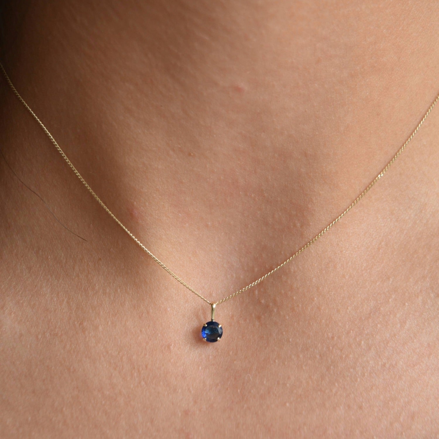 Solid 9ct gold September birthstone necklace with a small blue pendant, worn just below the collarbone.