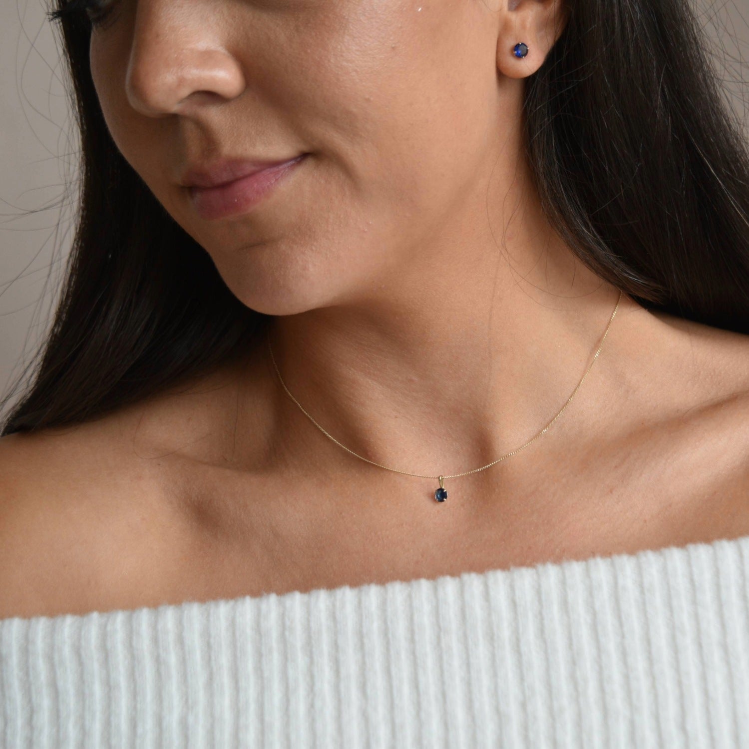 Solid 9ct gold September birthstone necklace worn below the collarbone above a pale off-the-shoulder top.