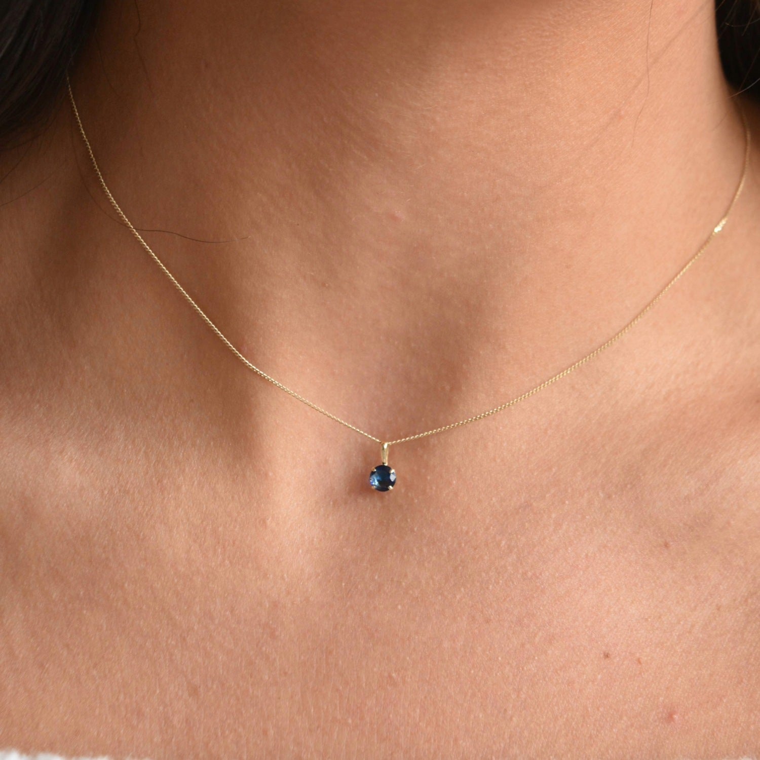 Close-up of a solid 9ct gold September birthstone necklace, showing its small blue pendant on a fine gold chain.