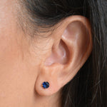 Close-up of a solid 9ct gold September birthstone stud earring, showing the round blue stone and gold setting.