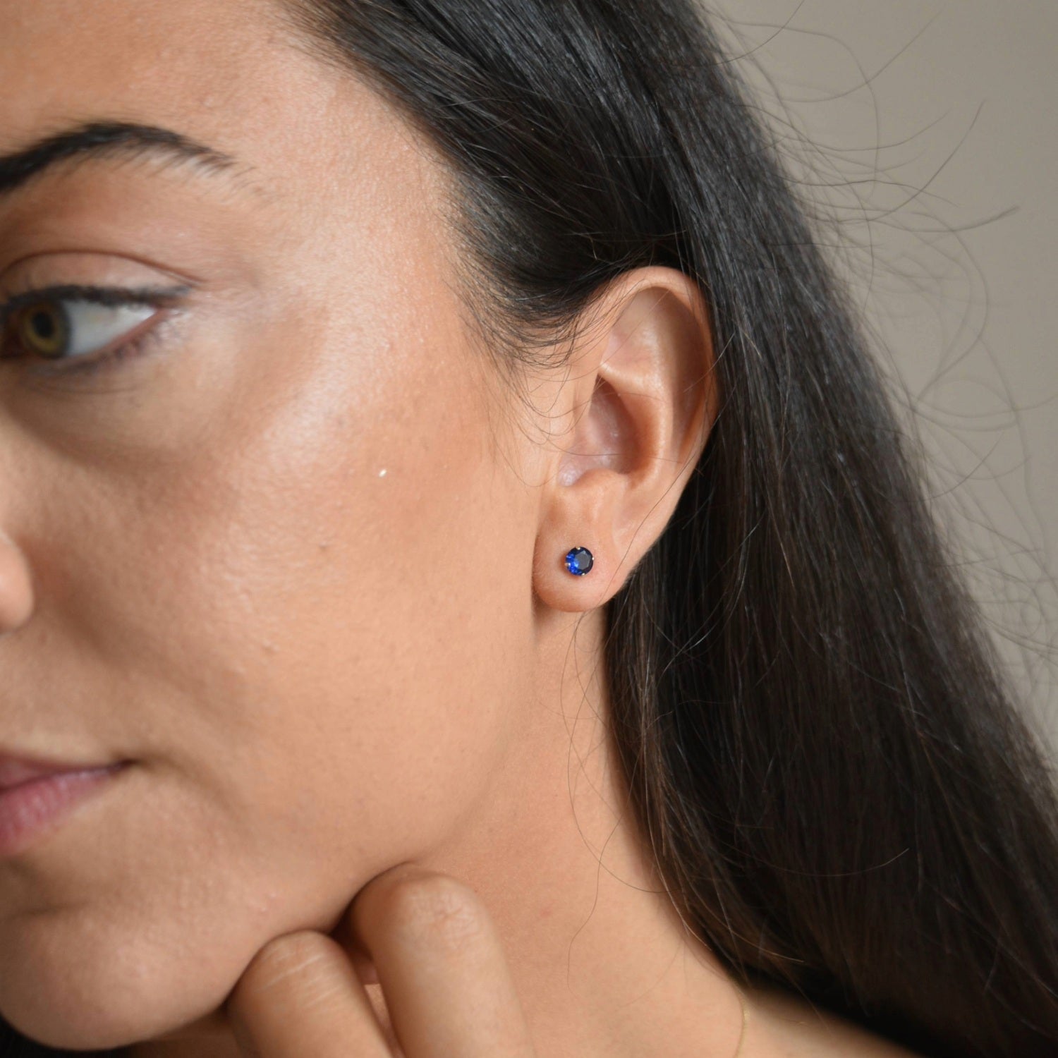 Side profile of a model wearing solid 9ct gold September birthstone stud earrings, showing their small size on the ear.