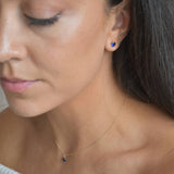 Solid 9ct gold September birthstone stud earrings shown on a model, with small blue stones sitting at the earlobes.