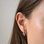Close-up of a sterling silver CZ star huggie earring worn on the ear, with a star charm suspended below the hoop.