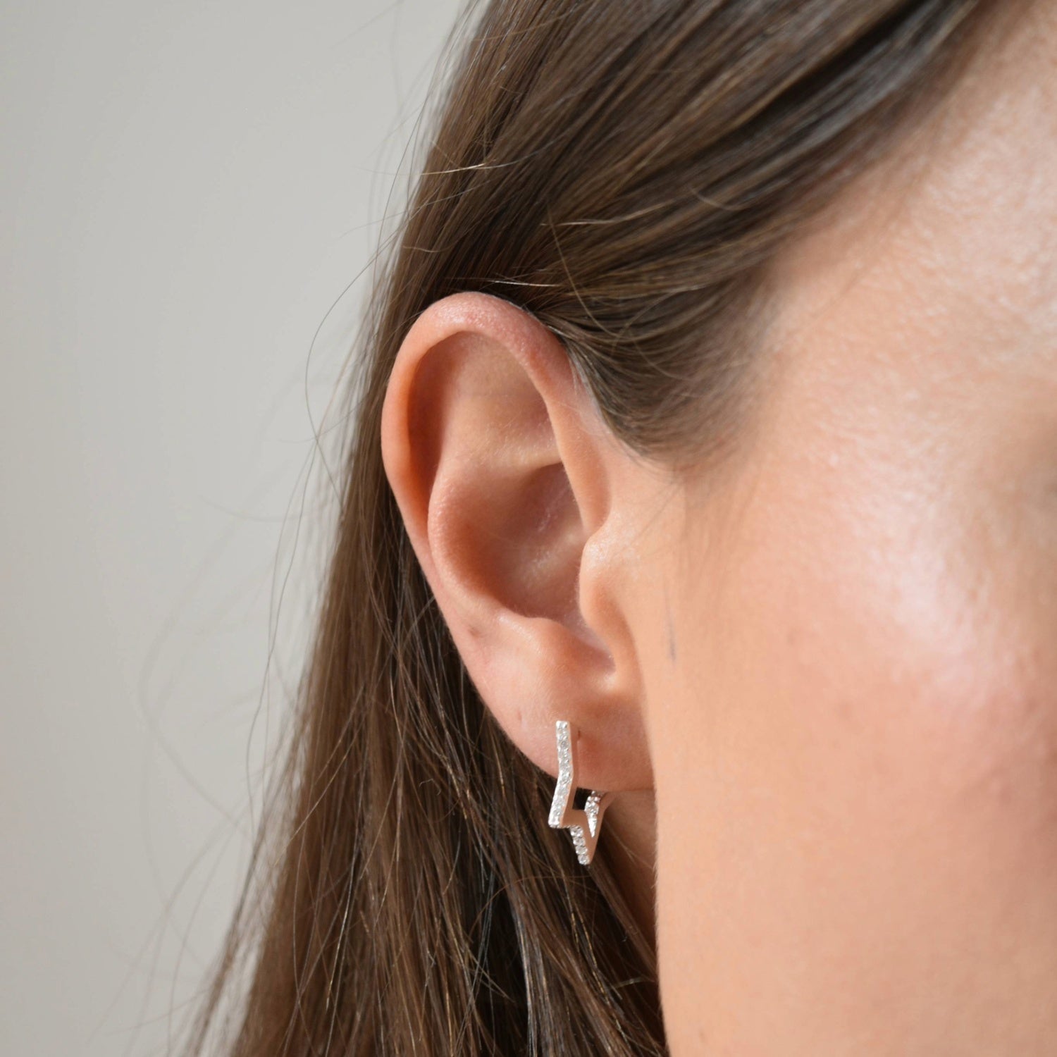 Close-up of a sterling silver CZ star huggie earring worn on the ear, with a star charm suspended below the hoop.