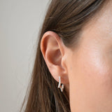 Close-up of a sterling silver CZ star huggie earring worn on the ear, with a star charm suspended below the hoop.