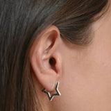 Side view of a sterling silver CZ star huggie earring, showing the small hoop and dangling star against the skin.