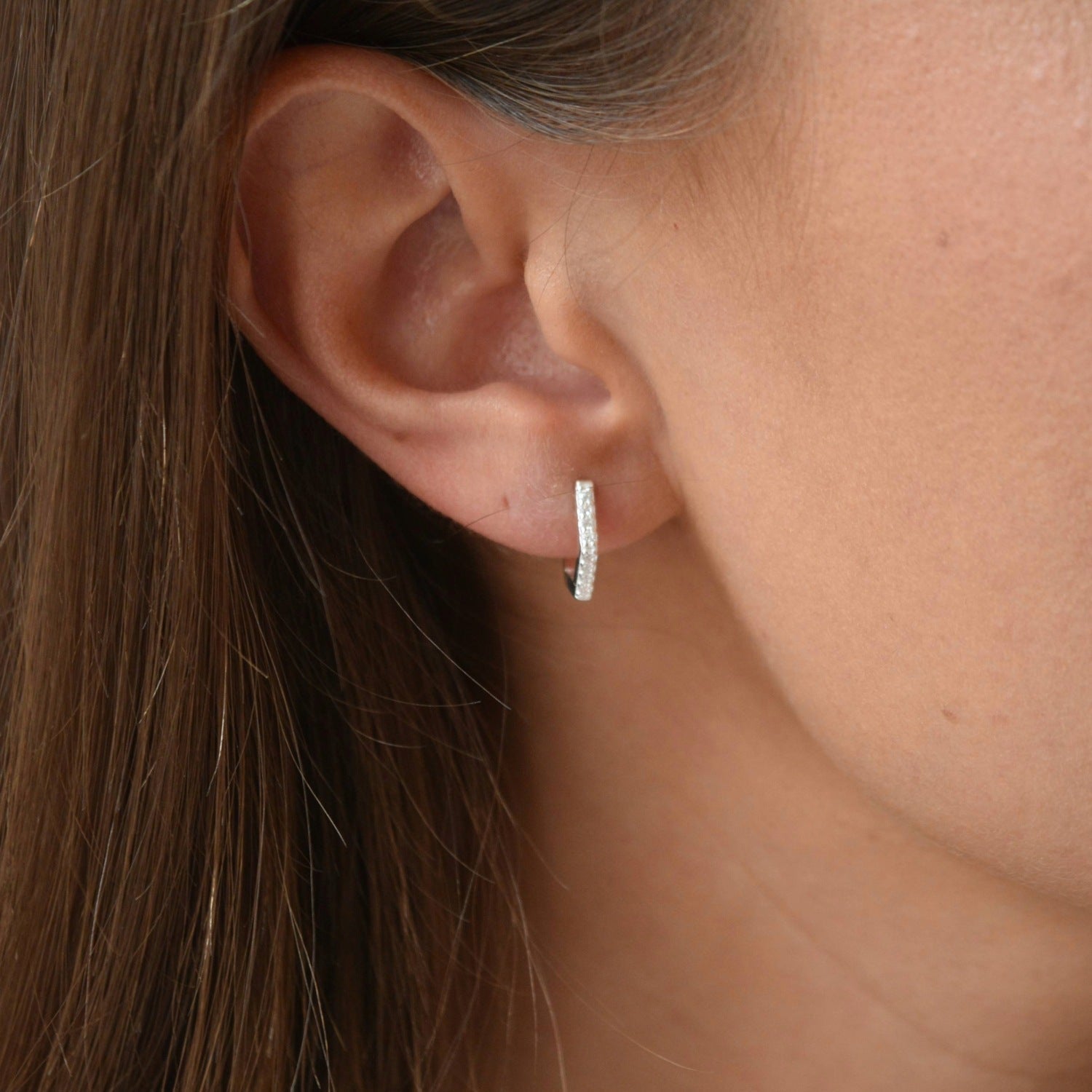 Side view of a sterling silver hexagon CZ huggie earring, showing how it sits around the earlobe.