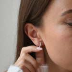 Sterling silver hexagon CZ huggie earrings worn by a model, with her hand raised beside the ear.