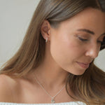 Sterling silver hexagon CZ huggie earrings shown on a model looking down, illustrating their size when worn.