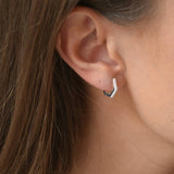 Close-up of a sterling silver hexagon huggie earring, showing its geometric shape and clear cubic zirconia stones.