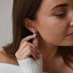 Sterling silver slim CZ huggie earrings worn by a model, showing the narrow hoops beside her fingertips.