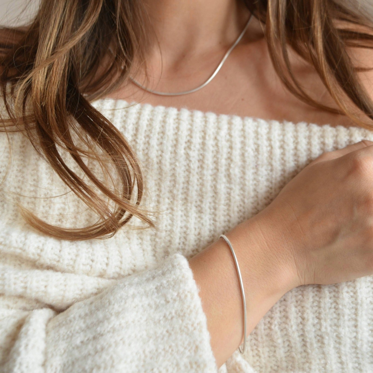 Sterling silver snake chain bracelet worn with the arm resting across a cream ribbed top, showing its slim proportions.