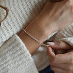 Close-up of a sterling silver snake chain bracelet worn on the wrist, with the other hand touching the chain.