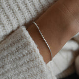 Sterling silver snake chain bracelet curving around the wrist beside a cream knitted sleeve.