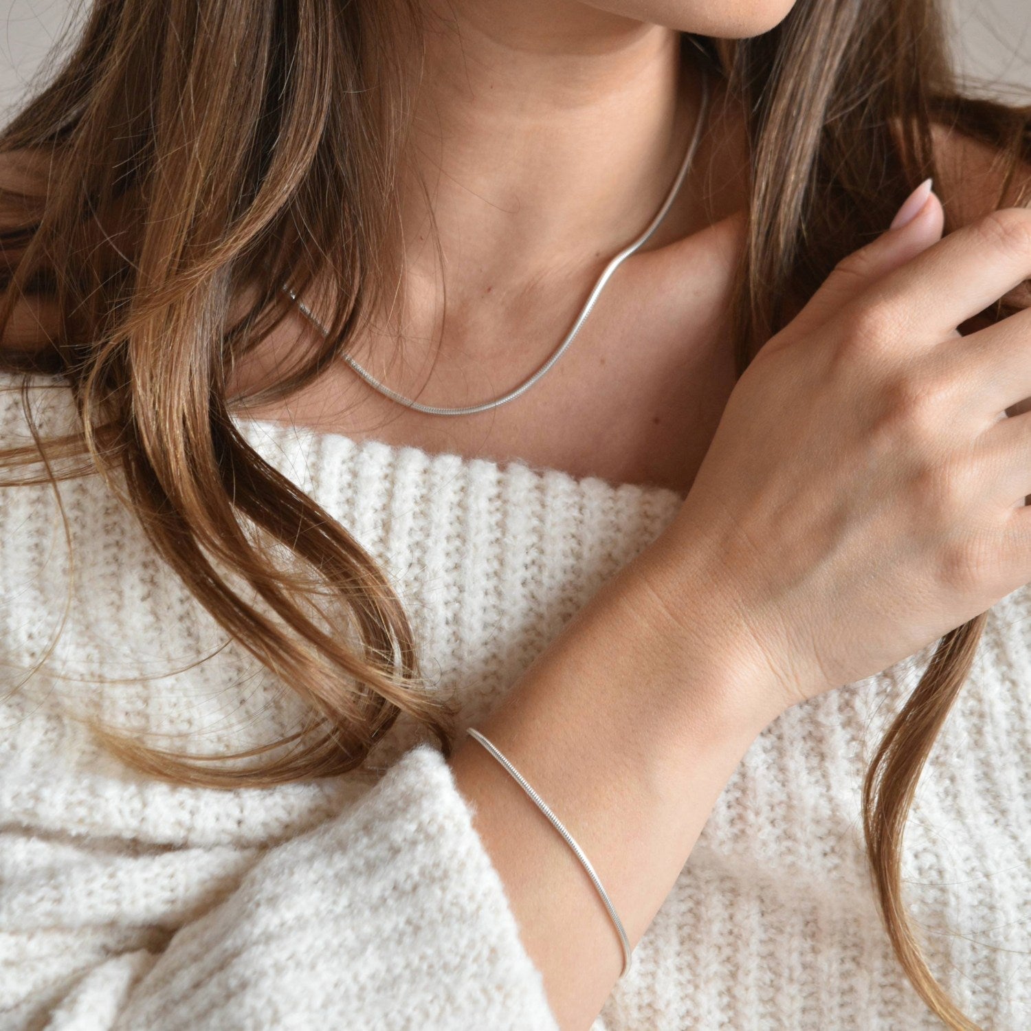 Sterling silver snake chain bracelet shown on a raised wrist, with the model’s hand resting near her shoulder.
